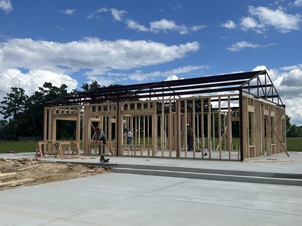 Barndominium under construction with exposed steel roof framing and timber wall studs on a concrete slab foundation.