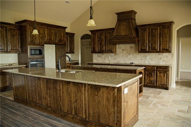 Finished barndominium kitchen featuring rustic wood cabinetry, granite countertops, a large central island, and tiled flooring.